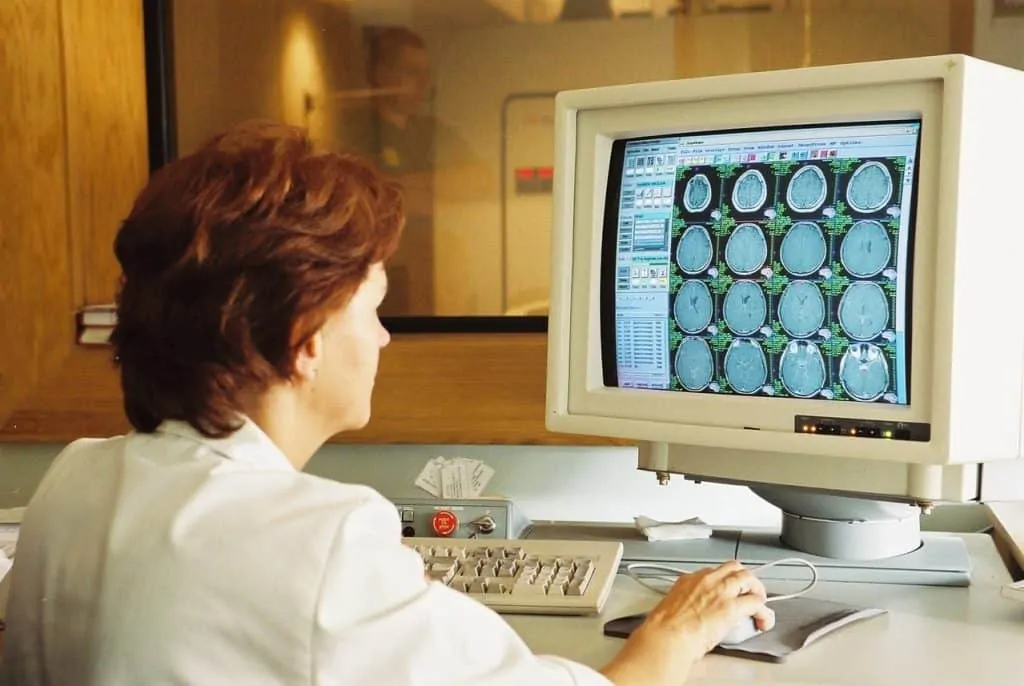 photo of person in white coat looking a screen with ct scans on it.