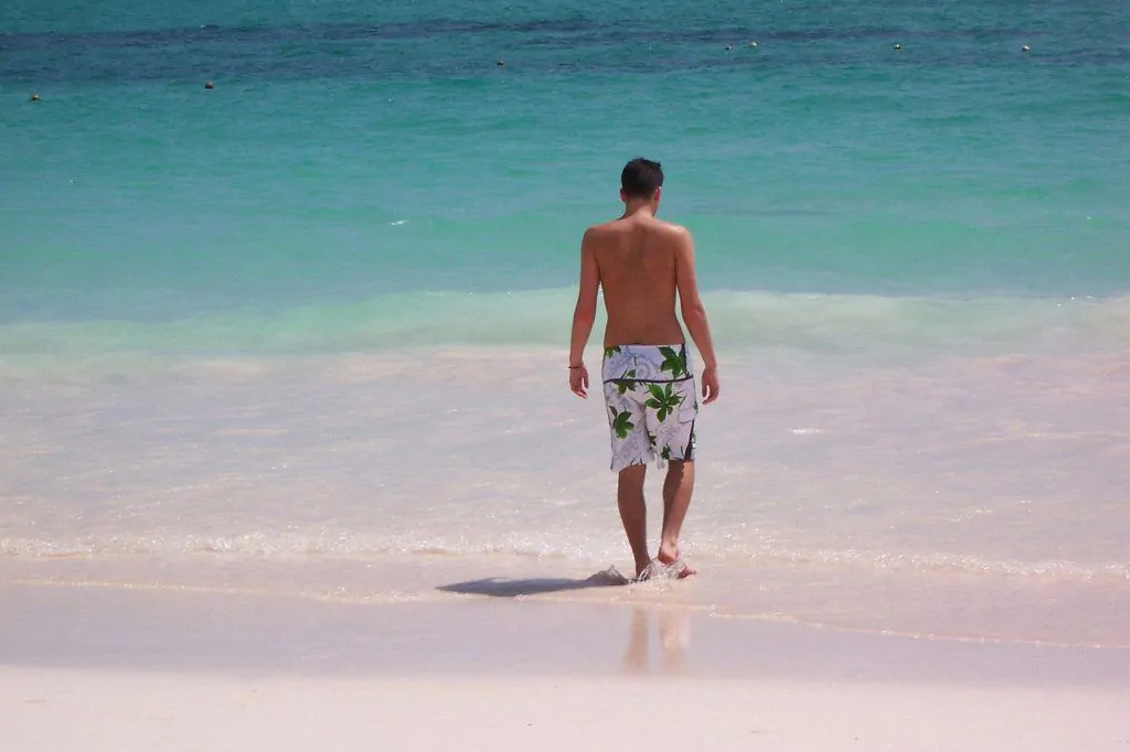 photo of man walking barefoot on a beach into the sea; ORIGINS OF EARTHING