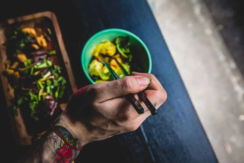 photo of a mans hand holding chopsticks and eating good from a bowl; Coimbra protocol diet.