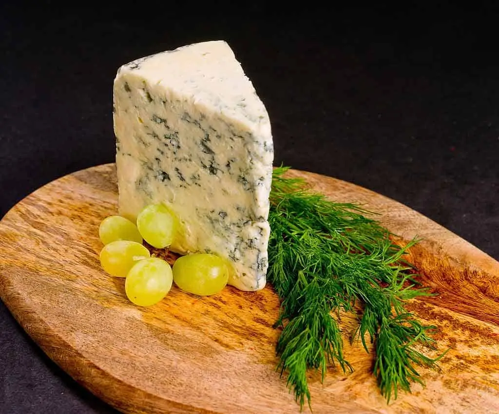photo of a cheese board with a wedge of blue cheese and some grapes and herbs; best dairy foods on a keto diet.