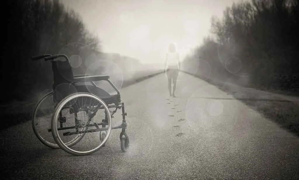 black and white photo of lady walking away from a wheelchair into the sunshine.